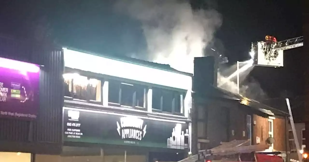 Firefighters wearing breathing gear tackle blaze near row of shops in Stockport