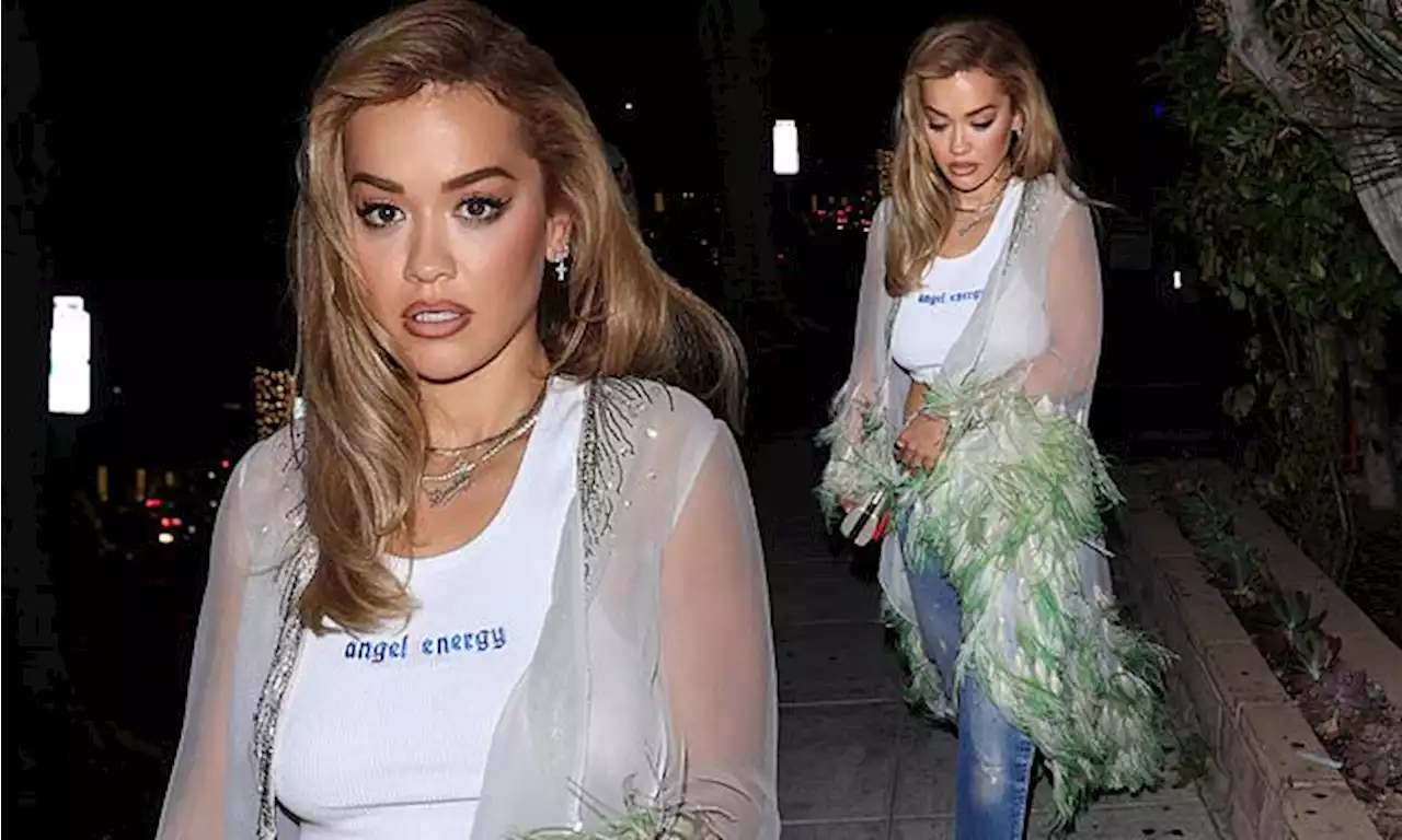 Rita Ora dons a white crop top and sheer shawl with green feathers