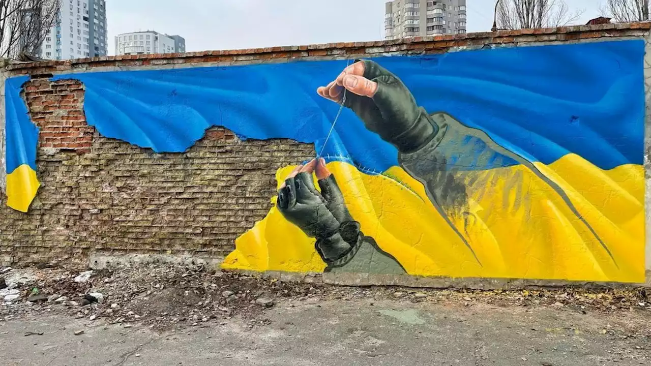 Un soldato cuce la bandiera ucraina: la street art per fermare la guerra