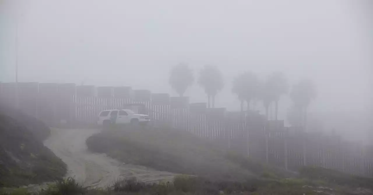 Cloaked by an ominous fog, a group of migrants swims to U.S. soil