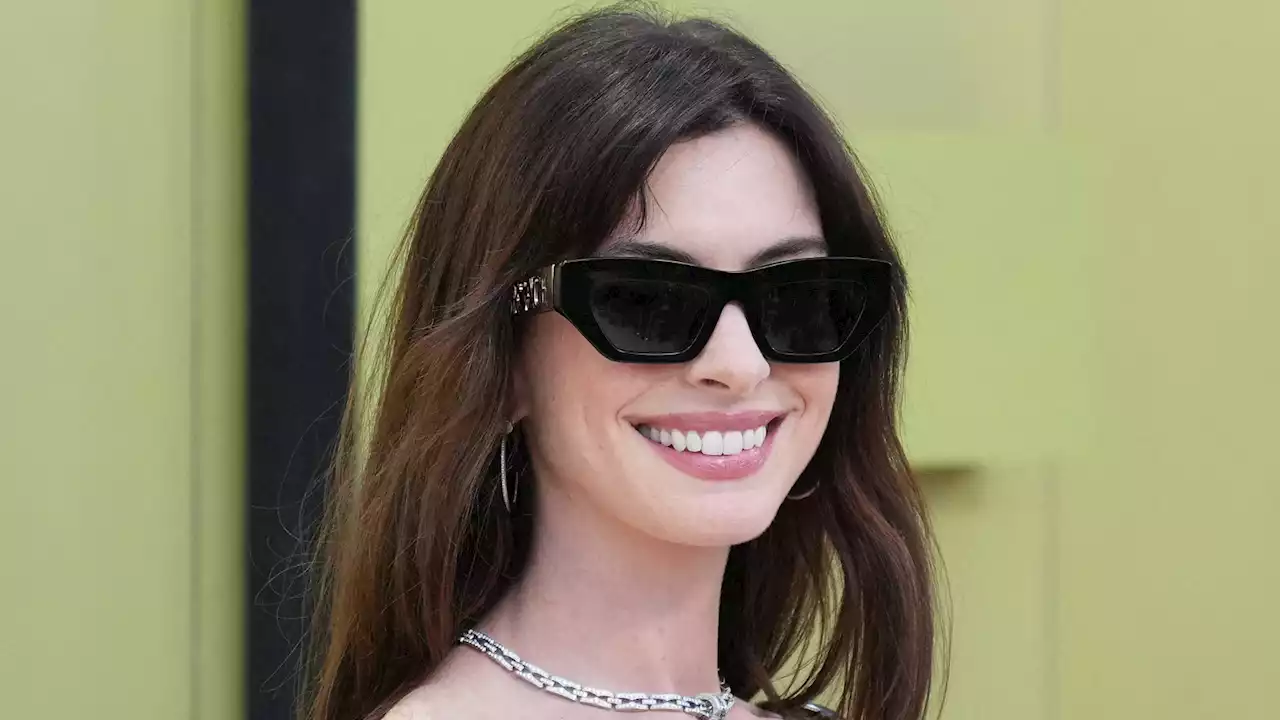 Anne Hathaway (40 ans) : lunettes de soleil noires et mini-robe en cuir, elle est plus sexy que jamais au défilé Versace !