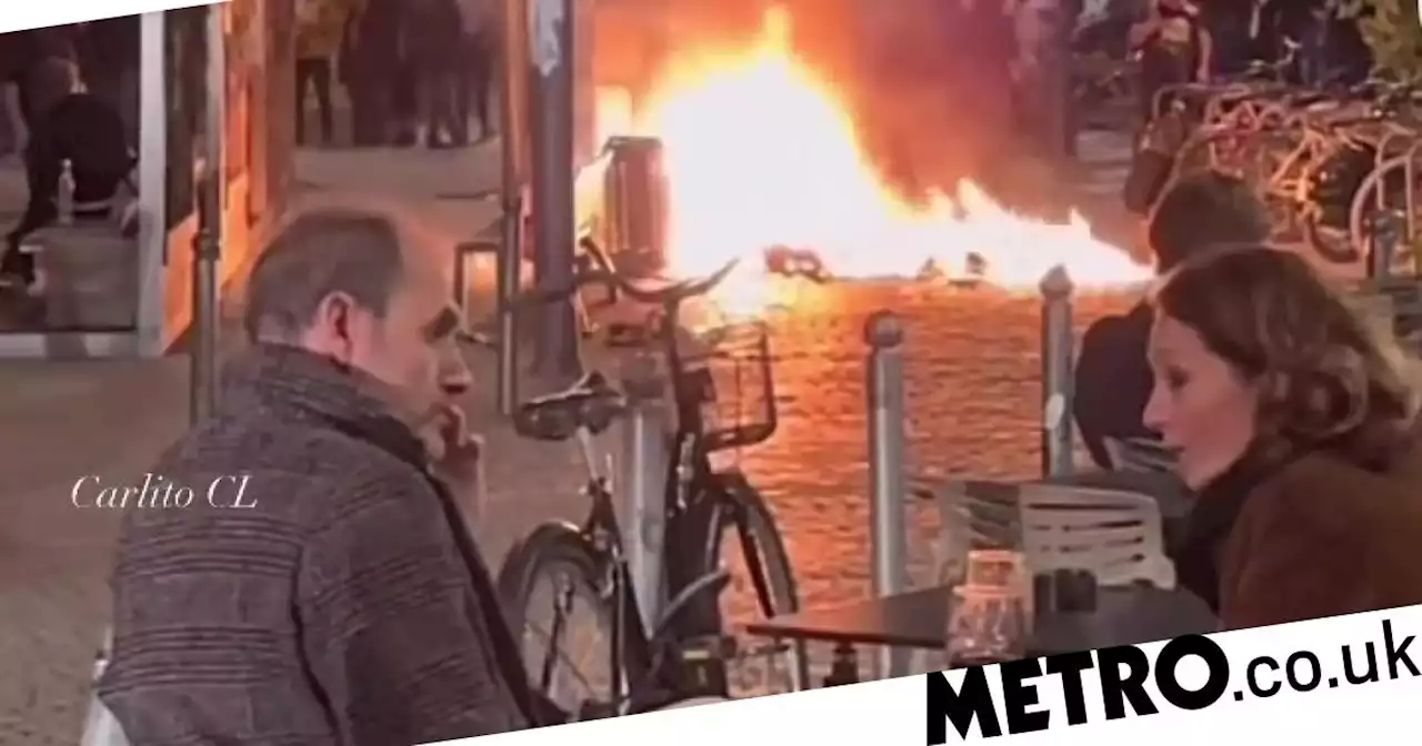 French couple enjoy glass of red wine as street burns behind them