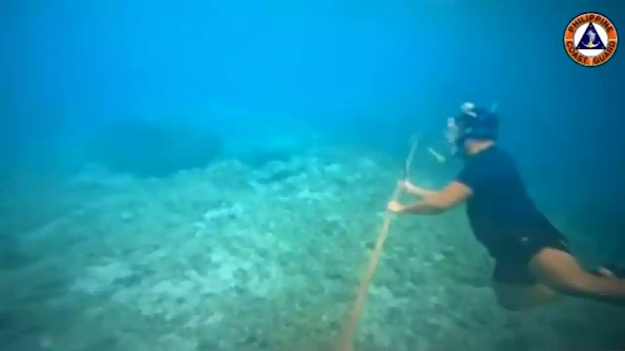 Filipino diver with a knife helps remove floating barrier installed by China in South China Sea