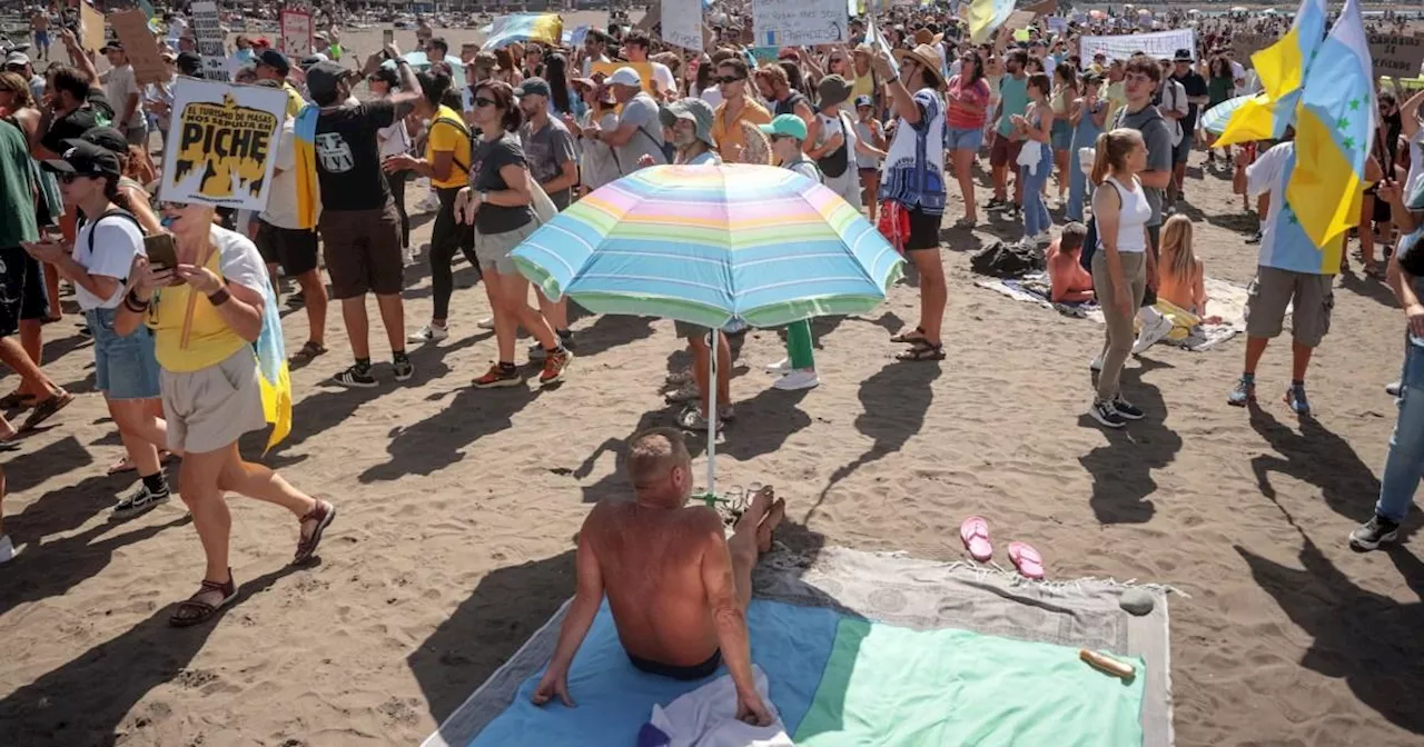 Holidaymakers look on as anti-tourism protesters march across the Canary Islands