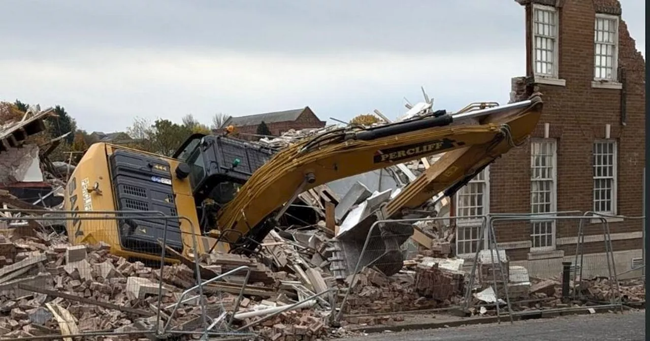 Digger demolishing building tips over in town centre