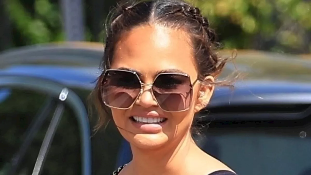 Chrissy Teigen rocks black sports bra and jeans as she is joined by husband John Legend to help...