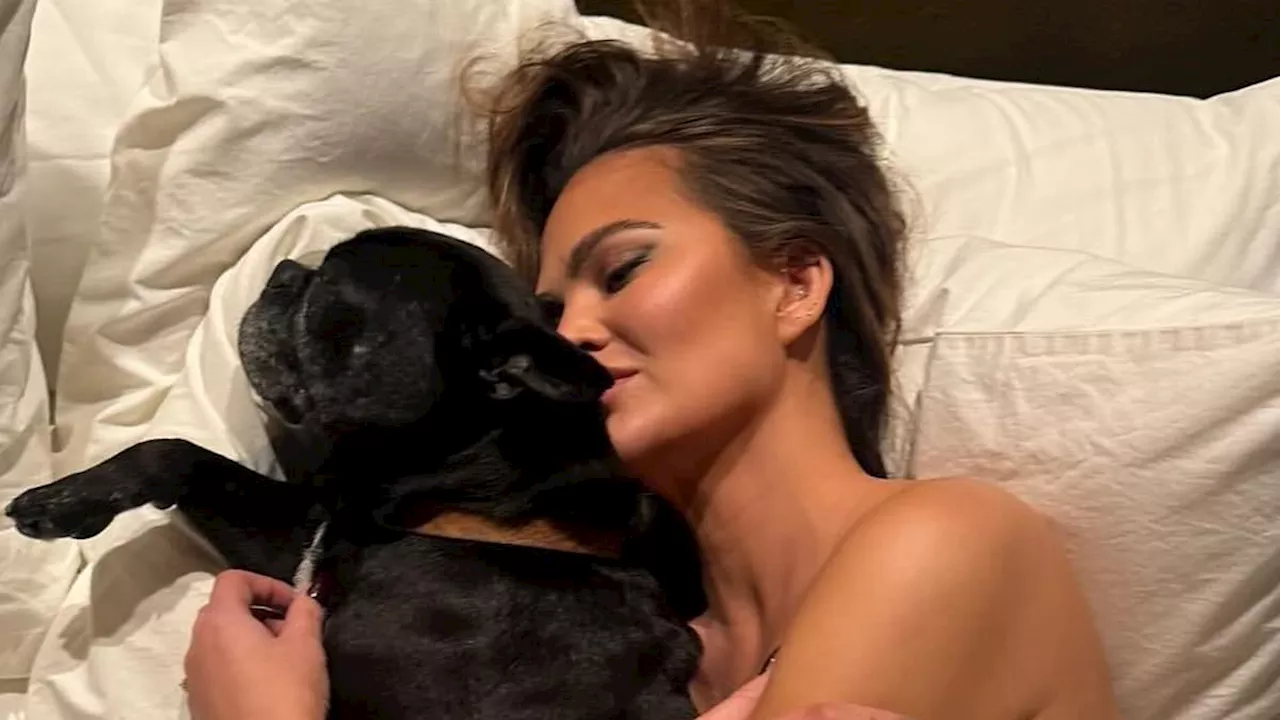 Chrissy Teigen poses TOPLESS while snuggling in bed with her dog in new photo... and reveals she...