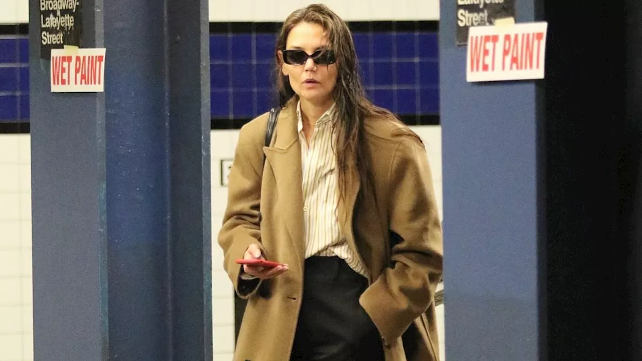 Katie Holmes leaves home with wet hair while looking casual chic in a tan overcoat as she rides the...