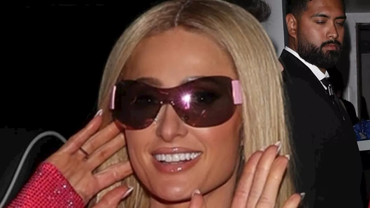 Paris Hilton puts on a leggy display in a sparkly pink mini dress and a personalised clutch bag as...