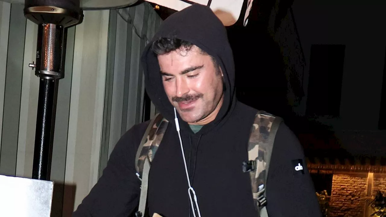 Zac Efron changes his look up with a mustache while going casual in a black hoodie as he leaves...