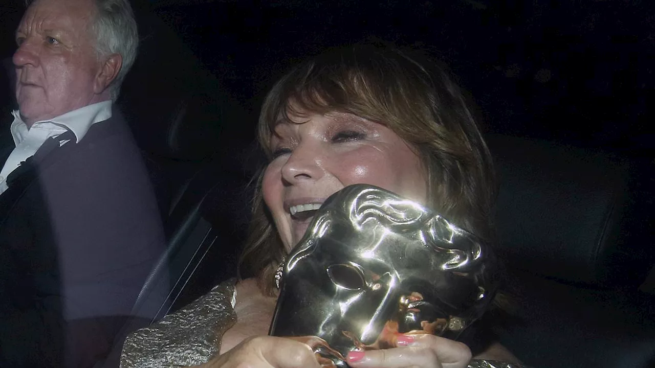 Bleary-eyed Lorraine Kelly proudly shows off her BAFTA TV gong as she heads home with her rarely...