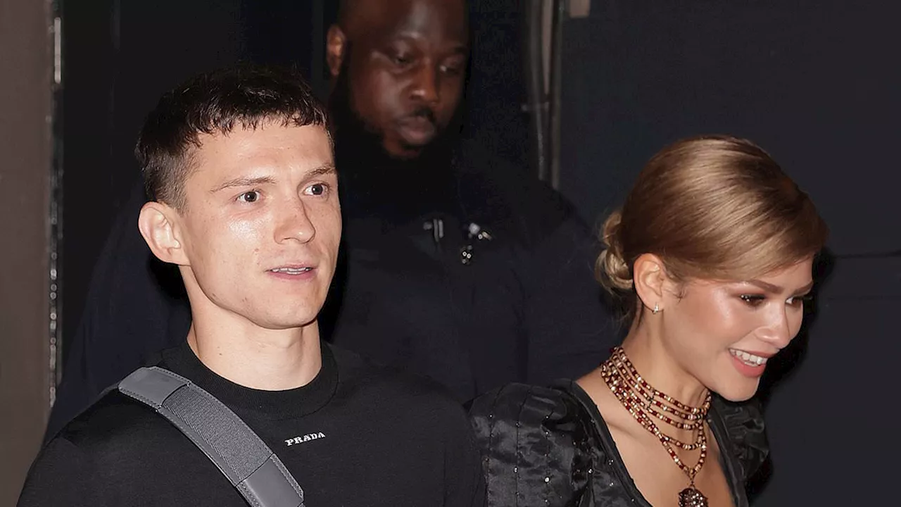 Tom Holland waves to fans while holding hands with his glamorous girlfriend Zendaya as she supports...