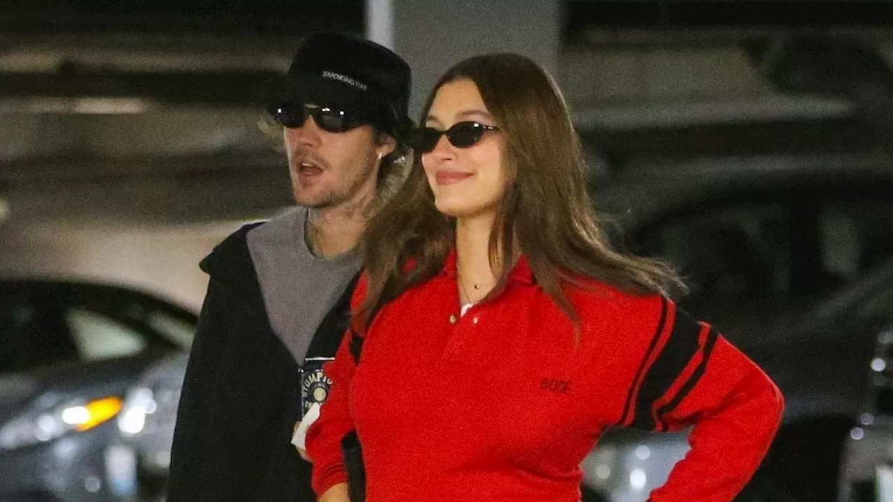 Hailey Bieber flashes her baby bump in a sizzling red sweater as she and husband Justin step out in...