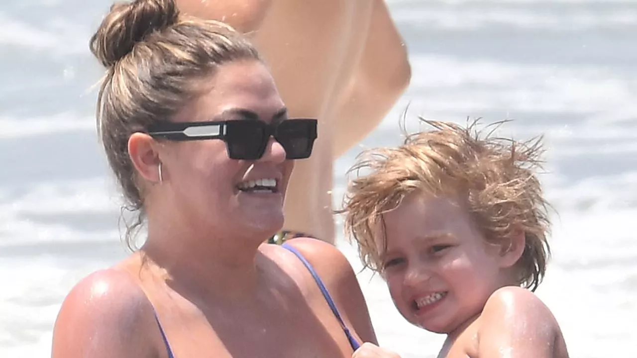 Brittany Cartwright is busty in a blue swimsuit as she splashes around on the beach with son Cruz,...