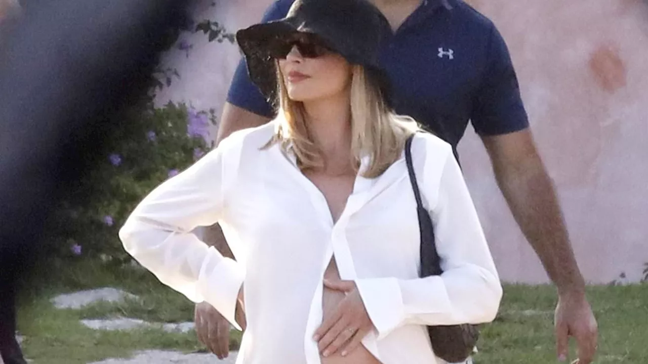 Pregnant Margot Robbie cradles her growing bump in a white unbuttoned shirt as she enjoys sweet...