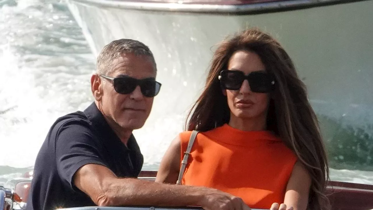 Amal Clooney looks glamorous in an orange jumpsuit as she leaves Venice with husband George after...